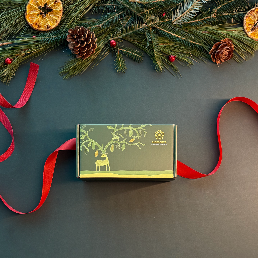Green gift box with reindeer design on a dark surface with red ribbon and Christmas decorations.