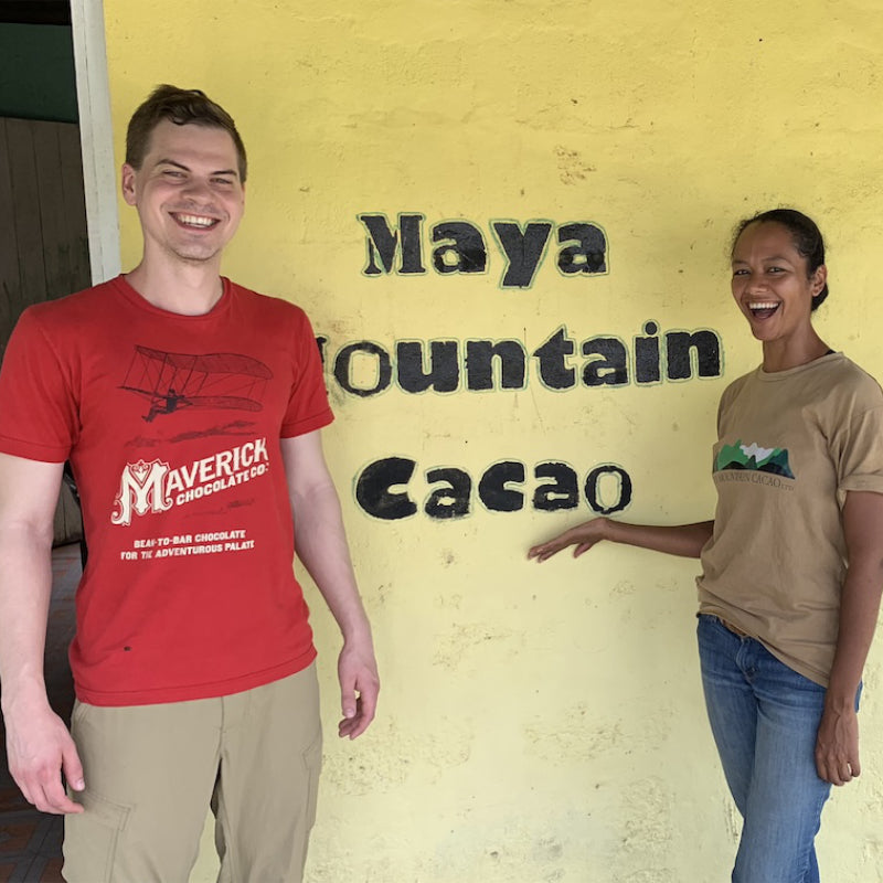 Two people standing in front of a yellow wall with 'Maya Mountain Cacao' text.