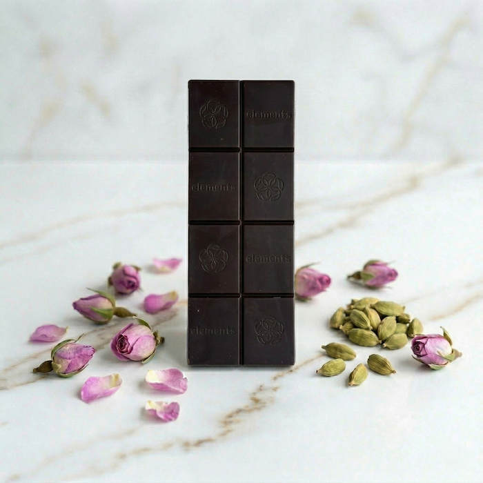 Dark chocolate bar with floral and cardamom elements on a marble surface